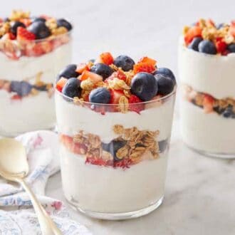Three yogurt parfaits with granola, blueberries, and strawberries.