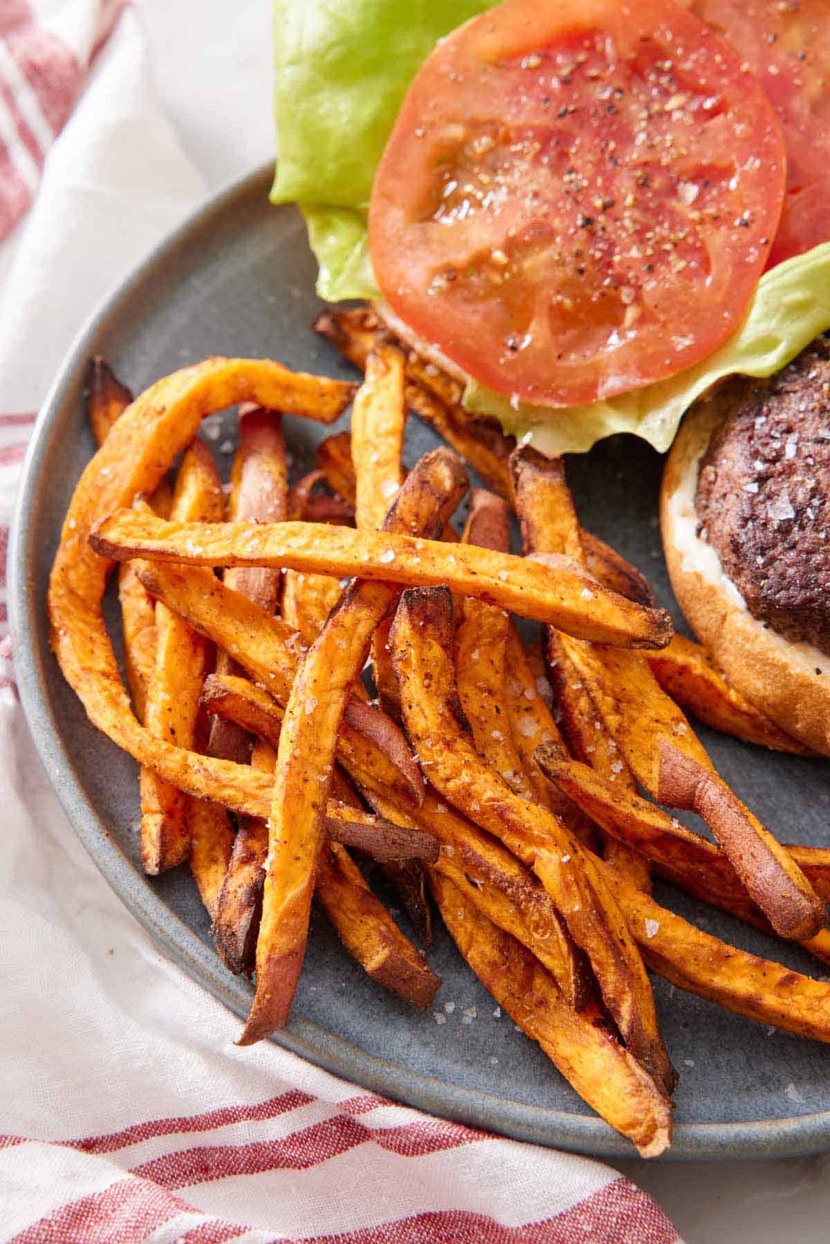 A plate with air fryer sweet potato fries with an opened burger beside it.