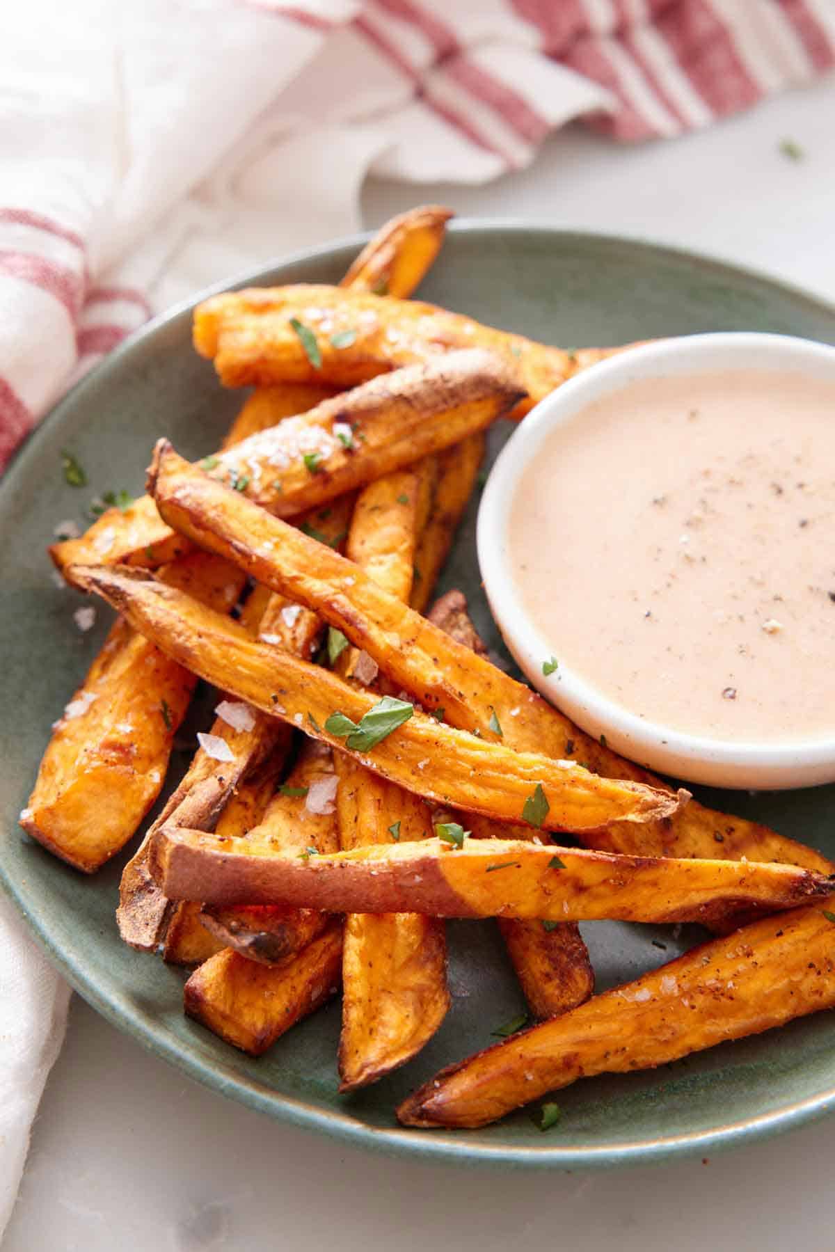 A plate with air fryer sweet potato fries with a bowl of dip.