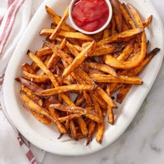 Overhead view of a platter of air fryer sweet potato fries with a bowl of ketchup with a linen napkin beside it.
