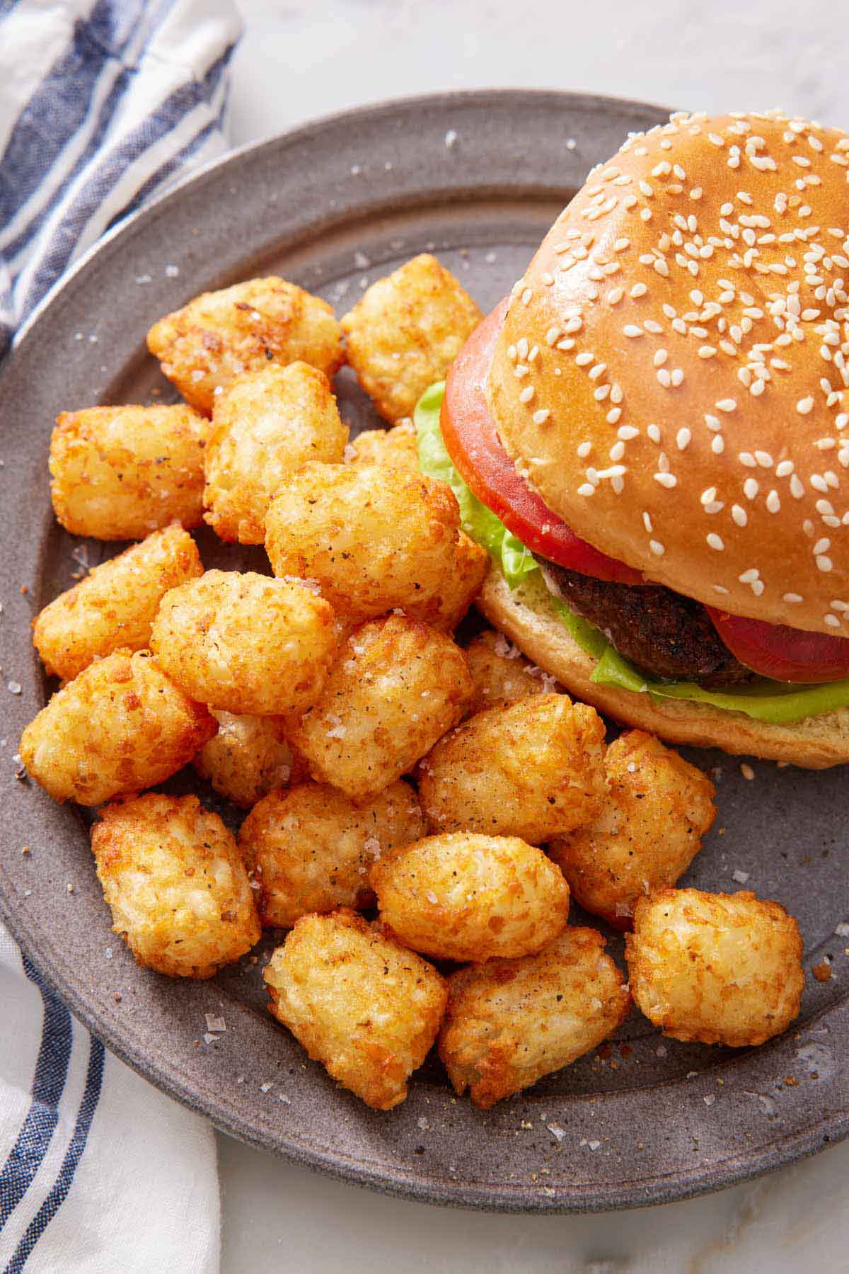 Overhead view of a plate of air fryer tater tots beside a hamburger.