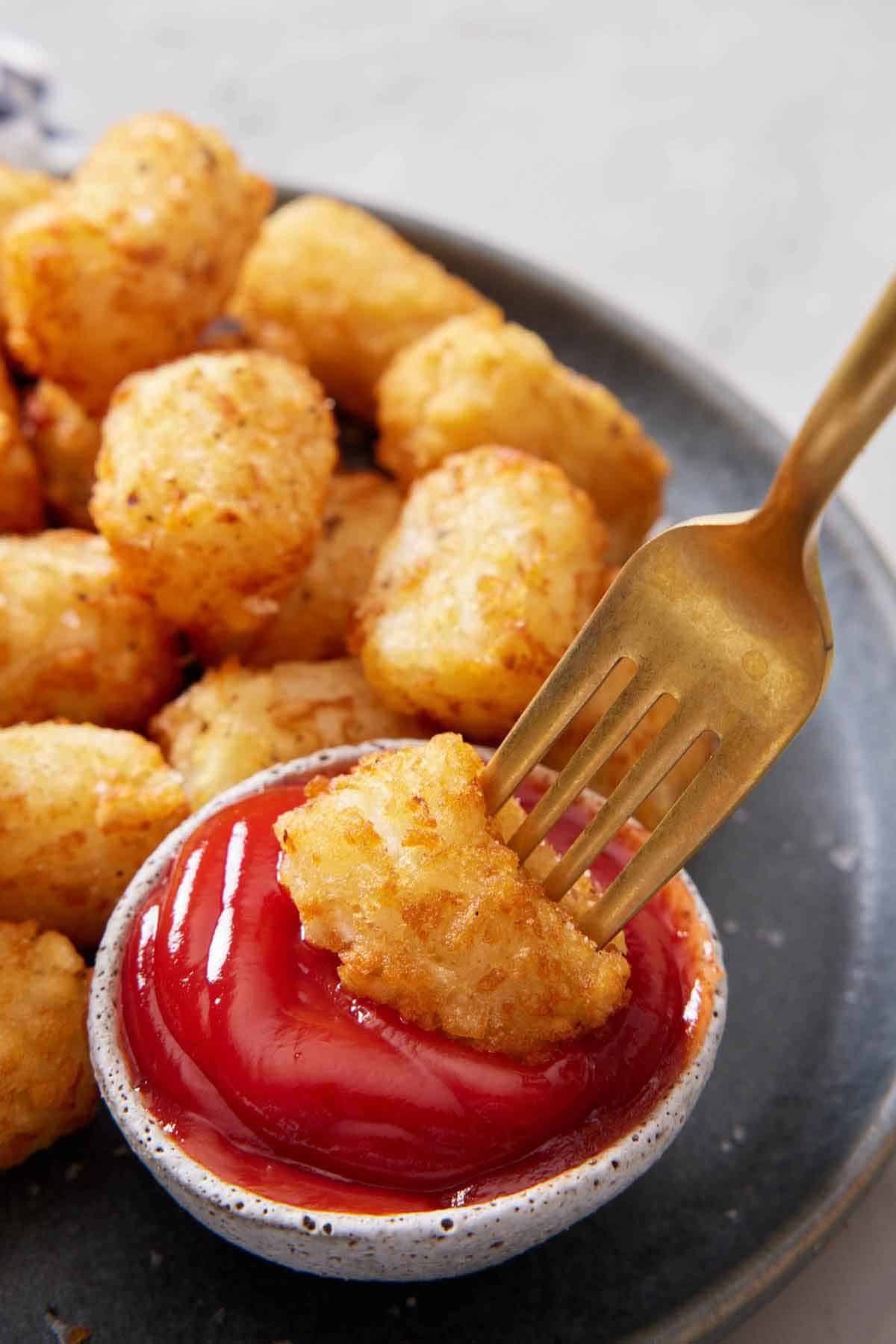 An air fryer tater tot on a fork dipped into ketchup.