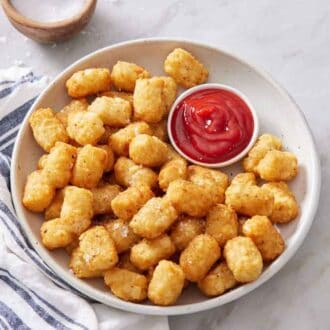 A large bowl of air fryer tater tots with ketchup. A linen napkin on the side along with a bowl of salt.