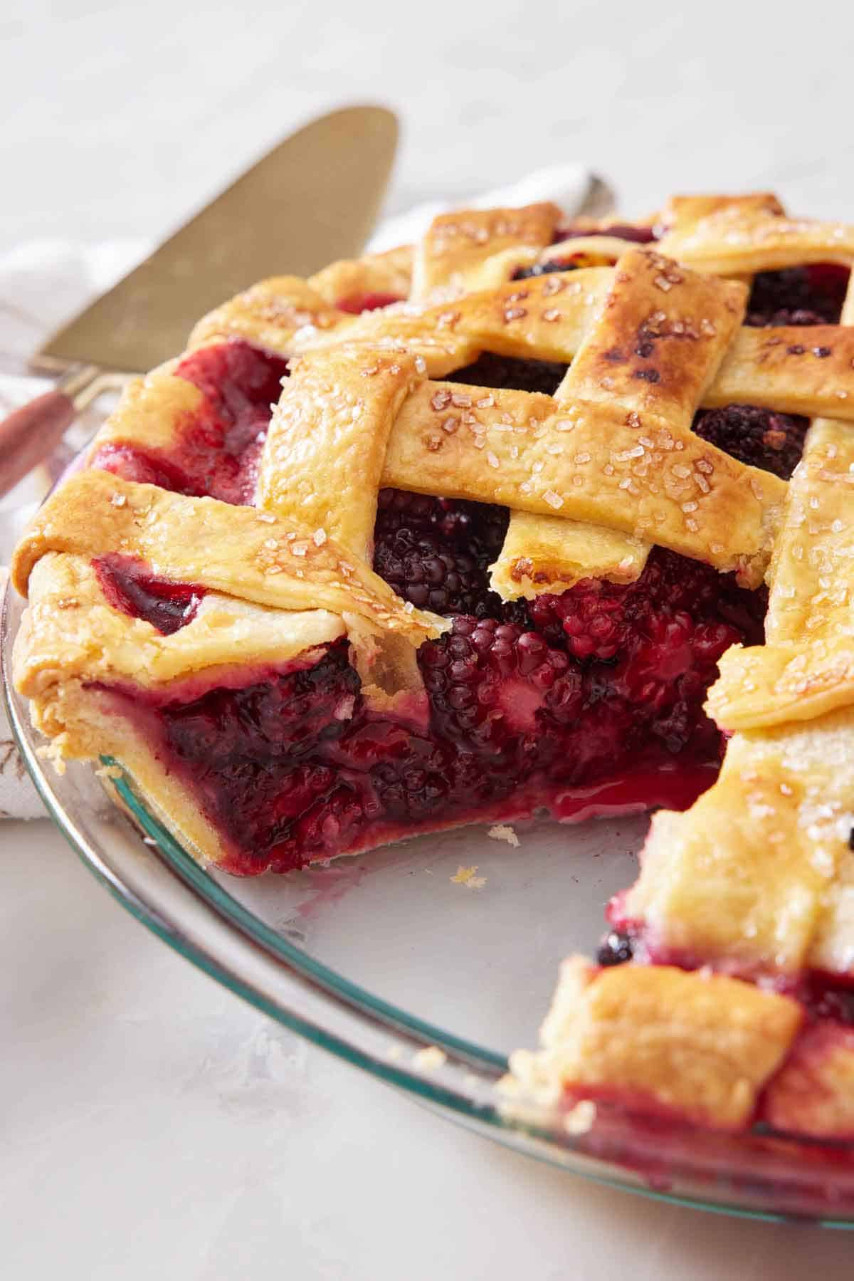 A close up view of a blackberry pie with a slice cut out, showing the berry-filled interior.
