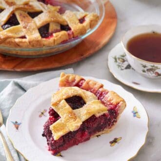Pinterest graphic of a plate with a slice of blackberry pie with the rest of the pie in the background along with a cup of tea.