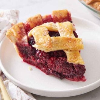 A slice of blackberry pie on a white plate with a fork beside it.