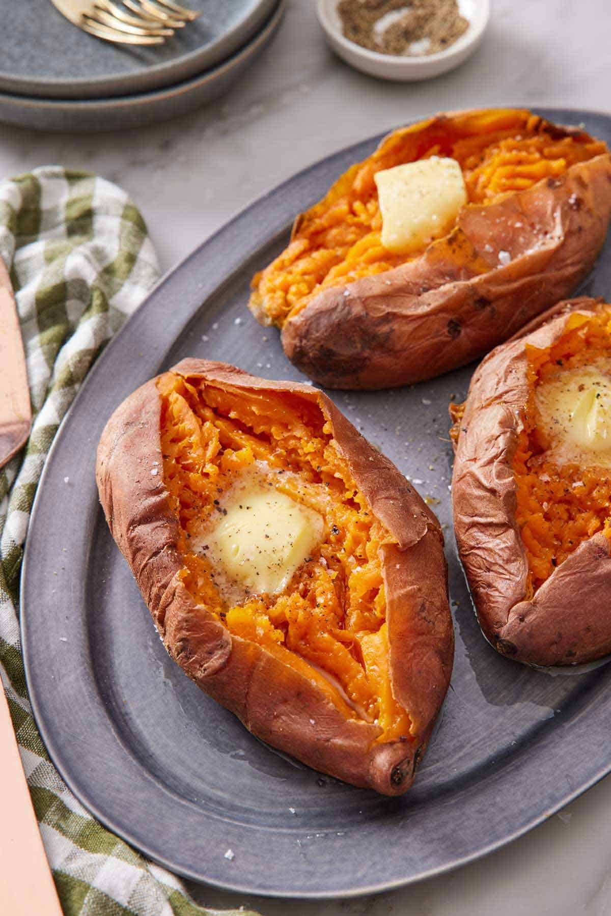 A platter with three instant pot sweet potatoes with a knob of butter on each. A green checkered napkin beside it.
