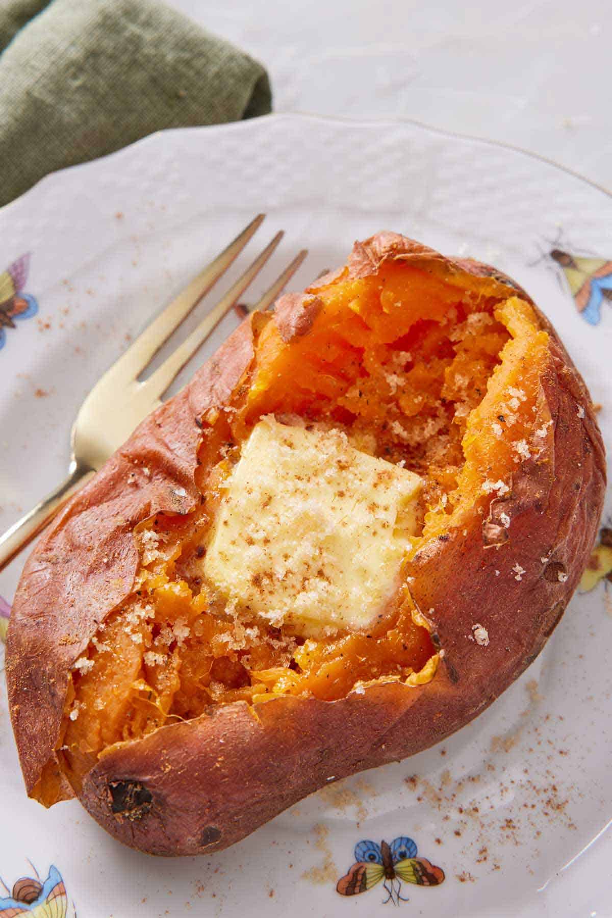 An instant pot sweet potato on a plate topped with a knob of butter and brown sugar.