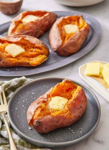 A plate with an instant pot sweet potato with a knob of butter in the middle. Three more with butter on a platter in the background.