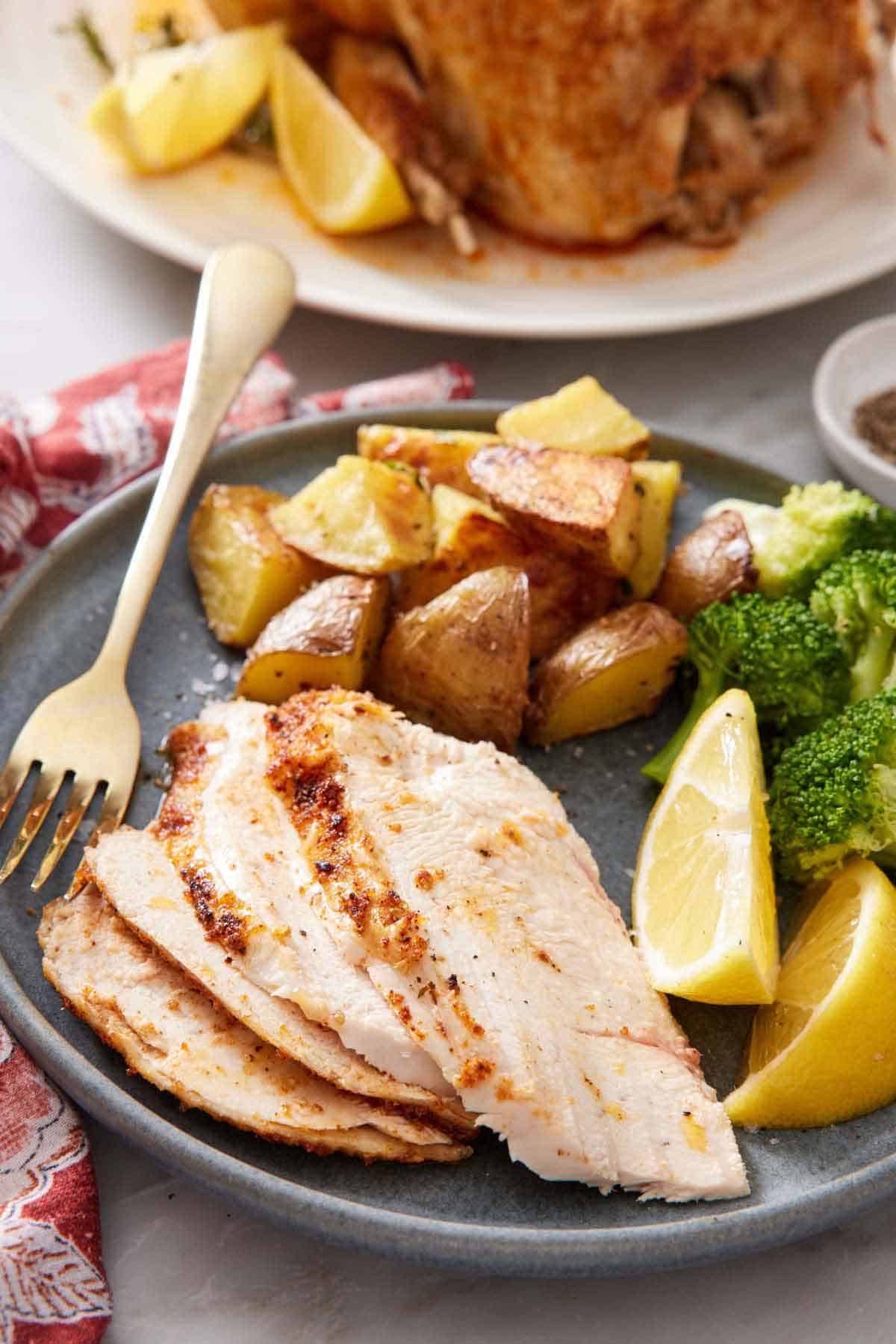 A plate with sliced instant pot whole chicken meat with roasted potatoes, lemon wedges, and broccoli.