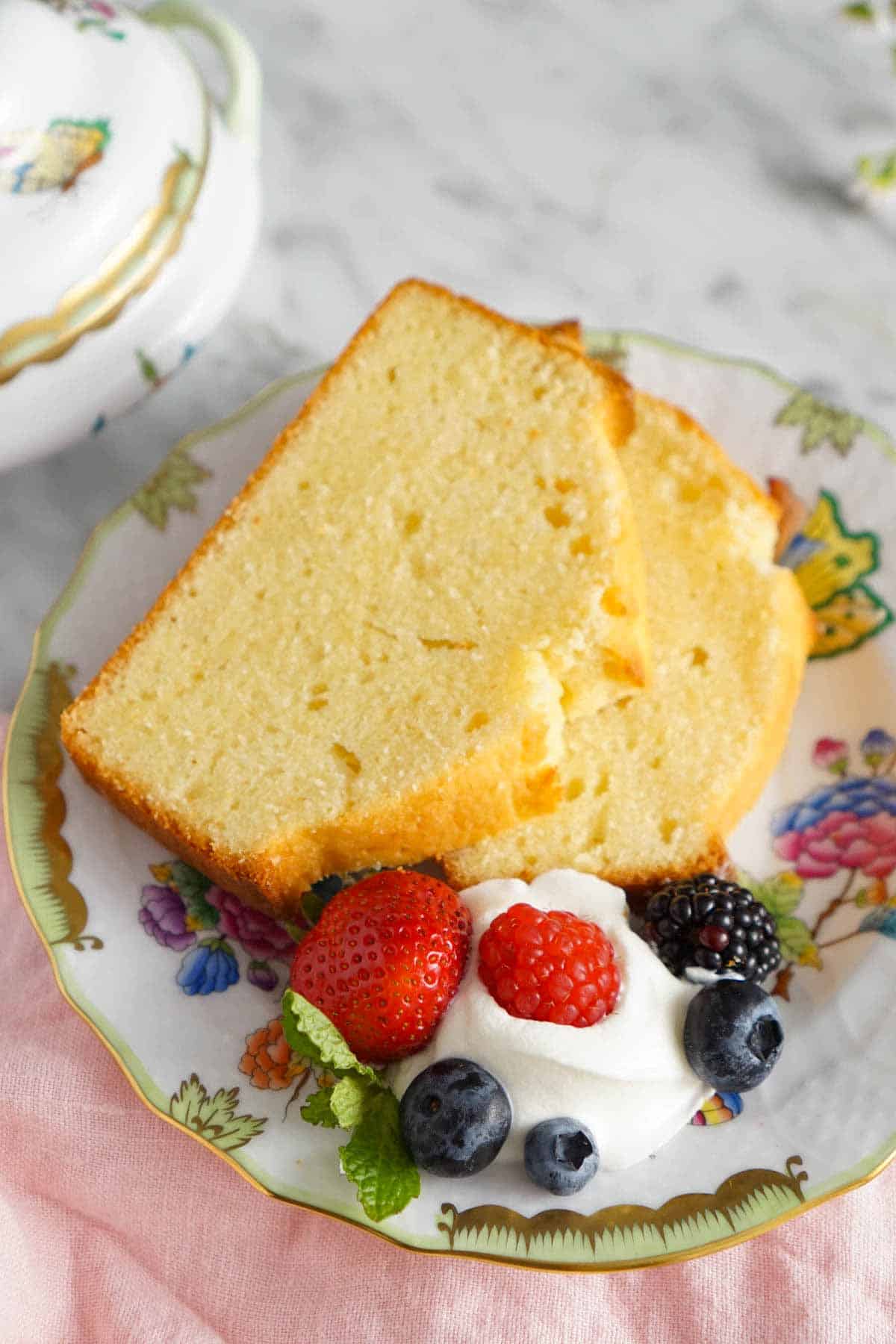 A plate with two slices of pound cake along with some whipped cream with berries on the side.