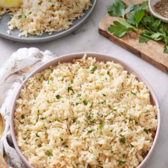 Pinterest graphic of a large plate of rice pilaf with chopped parsley garnish. Another plate in the background with rice pilaf along with a lemon wedge and meat.