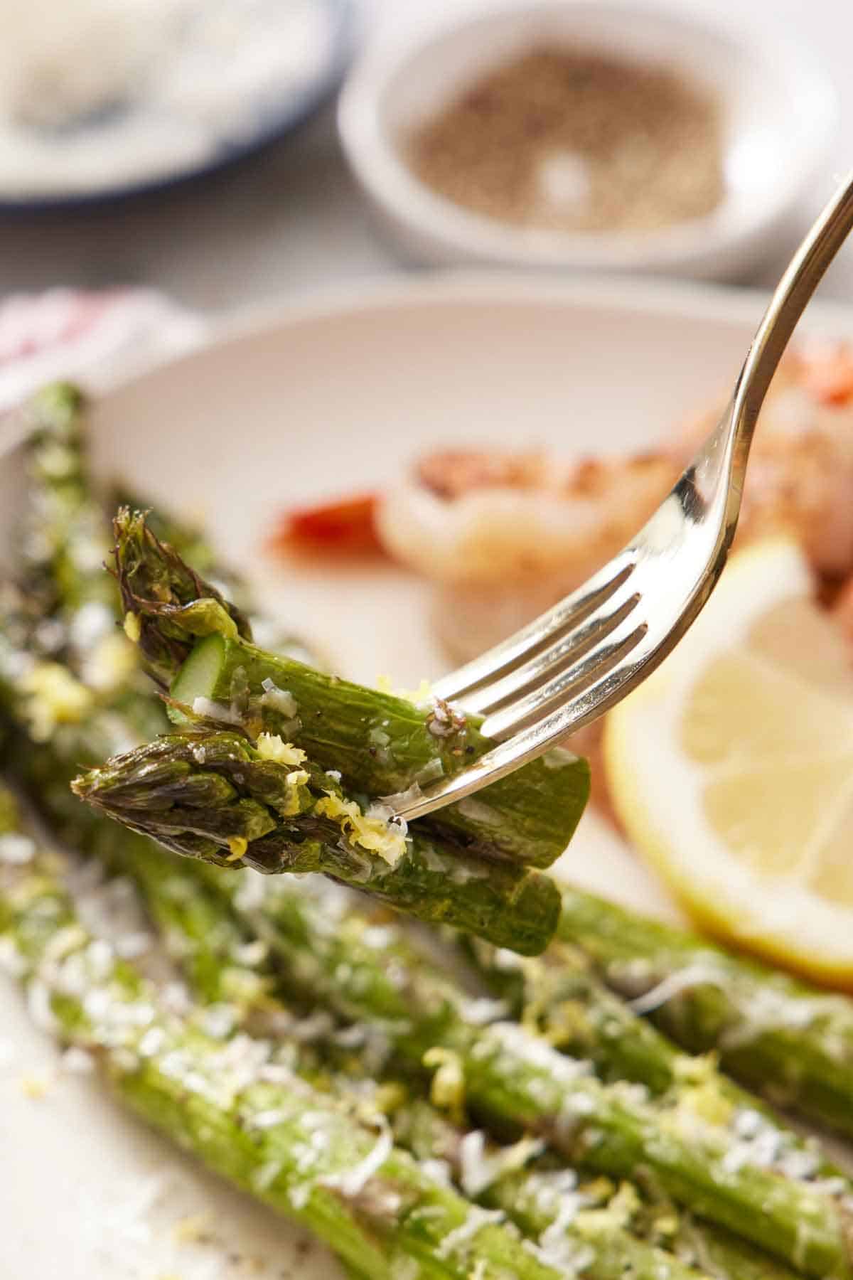 A fork holding up a bite of air fryer asparagus from a plate.