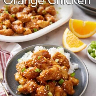 Pinterest graphic of a plate with air fryer orange chicken over rice. A platter in the background with more chicken. Orange wedges on the side.