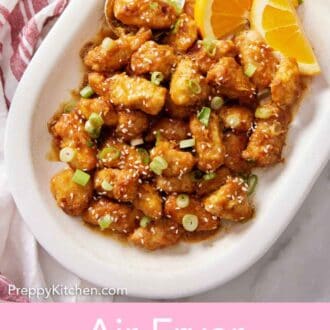 Pinterest graphic of an overhead view of a platter of air fryer orange chicken topped with green onions and sesame seeds with some orange wedges.