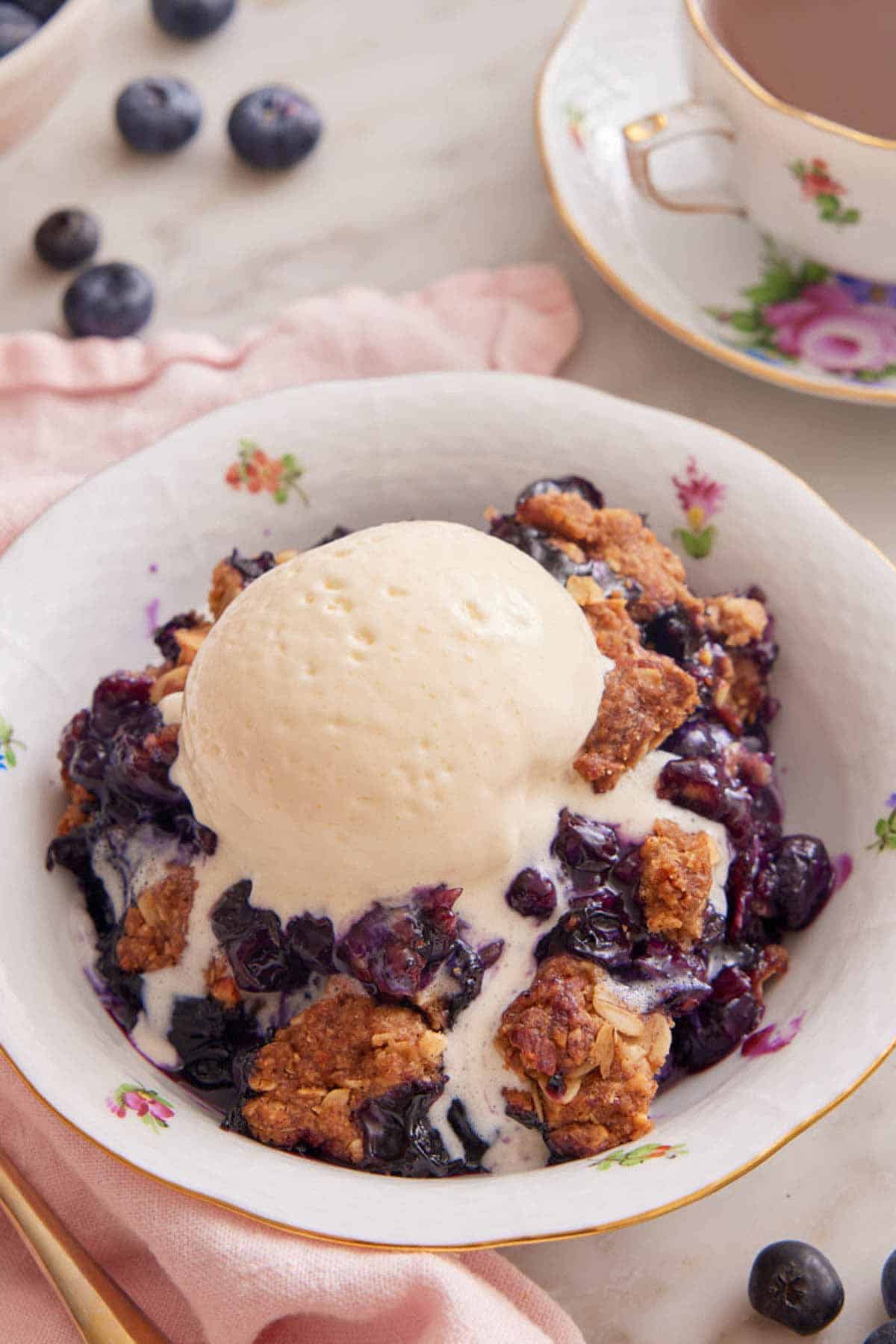 A plate with blueberry crisp with a scoop of vanilla ice cream melting on top.
