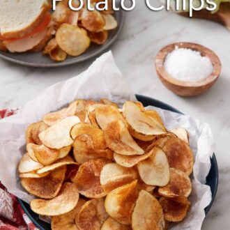 Pinterest graphic of a plate lined with parchment paper topped with homemade potato chips. A plate with a cut sandwich with chips in the back along with a bowl of salt and sandwich ingredients.