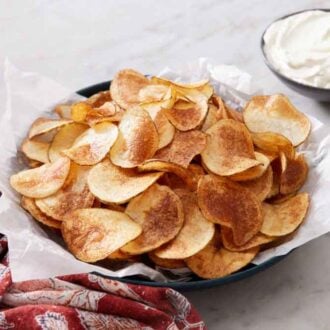 A parchment lined plate of homemade potato chips with a bowl of dip in the back.