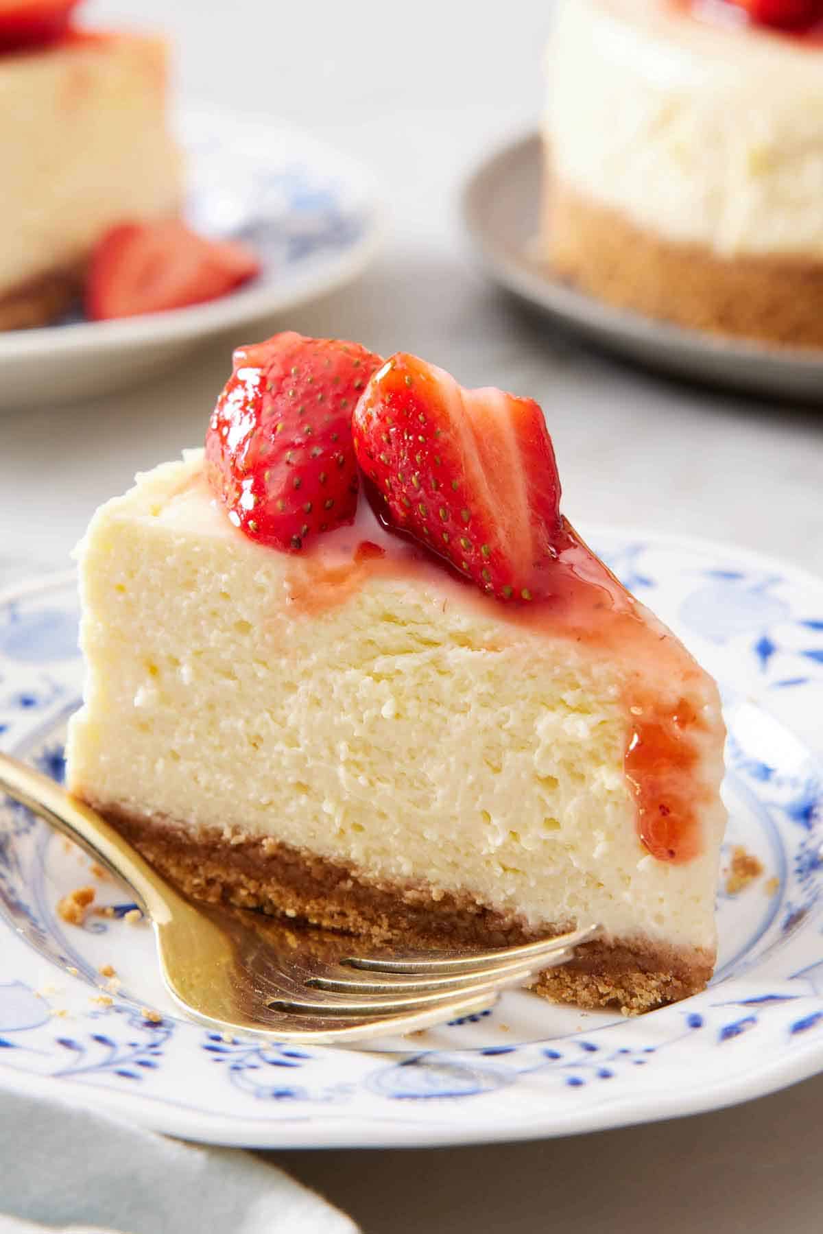 A plate with a slice of Instant Pot cheesecake topped with strawberries with a fork beside it.