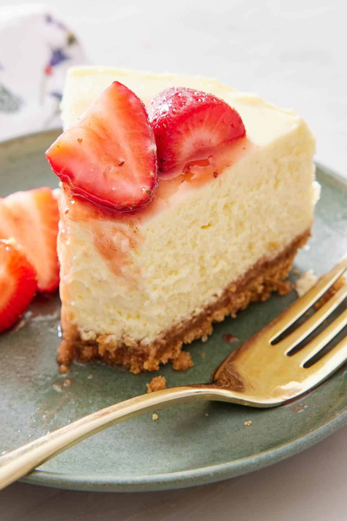 A close up view of a slice of Instant Pot cheesecake with the tip eaten. Strawberries on top.
