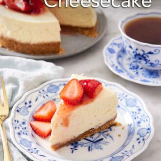 Pinterest graphic of a plate with a slice of Instant Pot cheesecake topped with chopped strawberries. A mug of tea and the rest of the cheesecake in the background.
