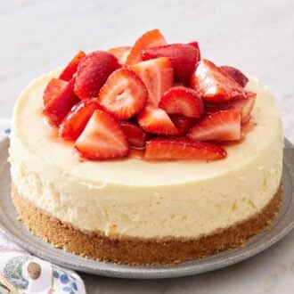 An Instant Pot cheesecake on a plate topped with chopped strawberries. A cake spatula on the side.