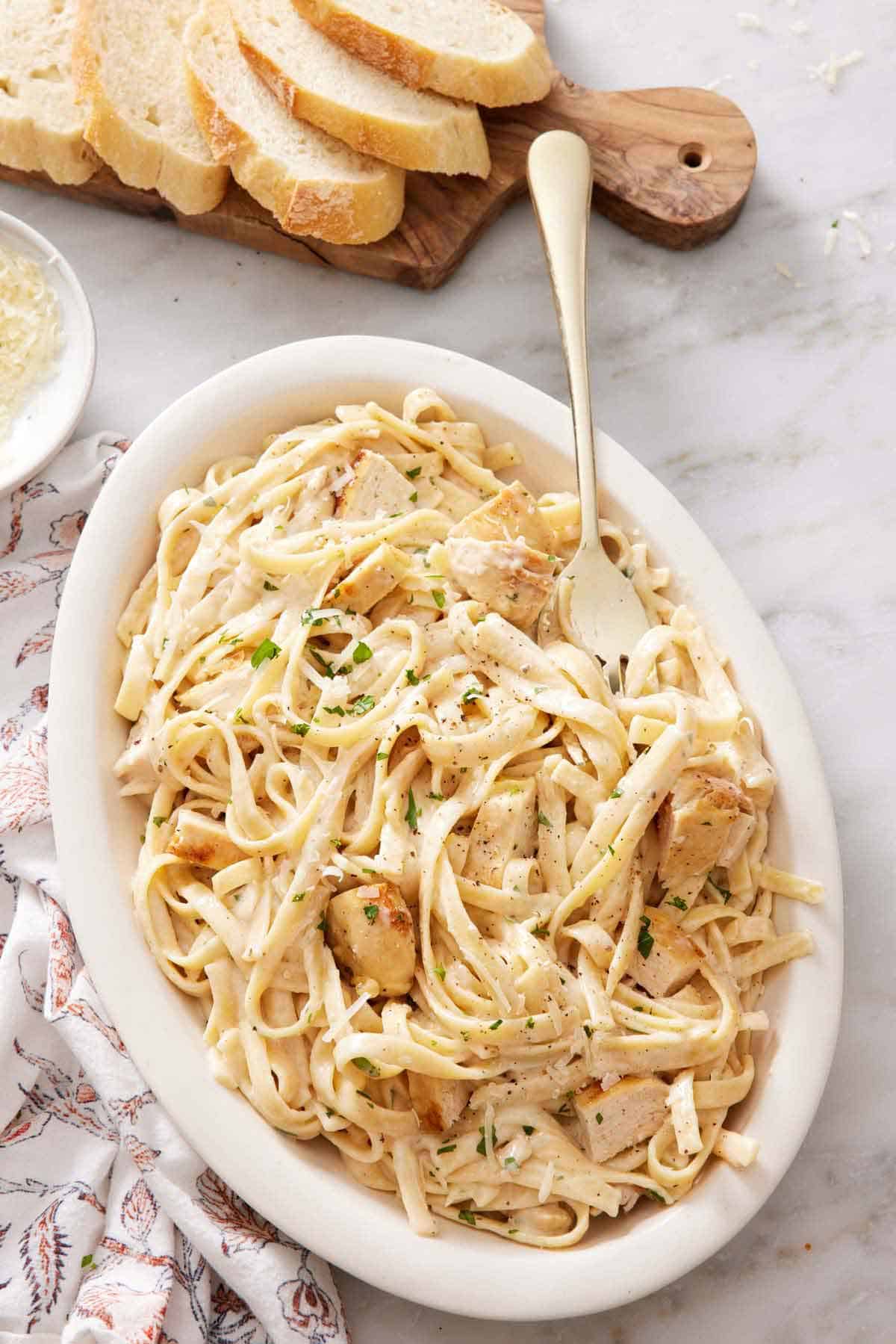 A serving platter of Instant Pot chicken alfredo with a fork. Sliced bread in the back.