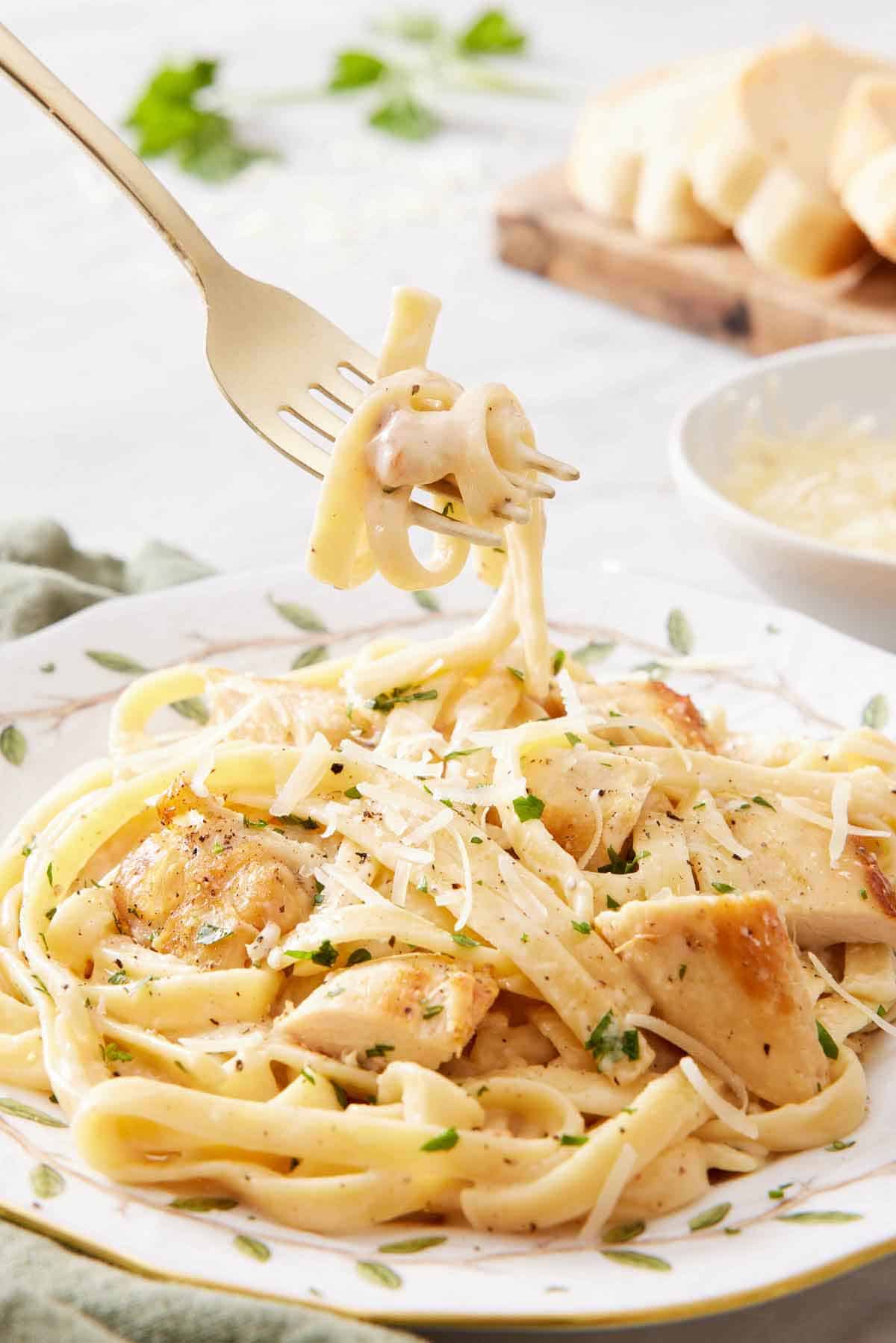 A fork lifting up a bite of Instant Pot chicken alfredo from a plate.