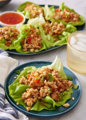 A plate with a lettuce wrap with more in the back on a platter with an iced drink.
