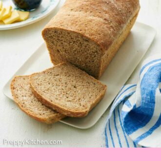 Pinterest graphic of a loaf of rye bread with two slices cut. A plate with jam and butter in the background.