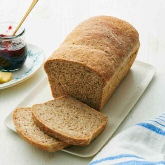 A loaf of rye bread with two slices cut from it. A jar of jam and some butter in the background.
