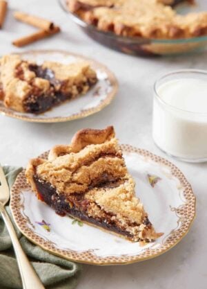 A plate with a slice of shoofly pie with a glass of milk, another plated serving, and the rest of the pie in the background.