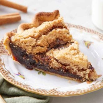 A plate with a slice of shoofly pie. A fork on the side with a glass of milk and cinnamon sticks in the background.