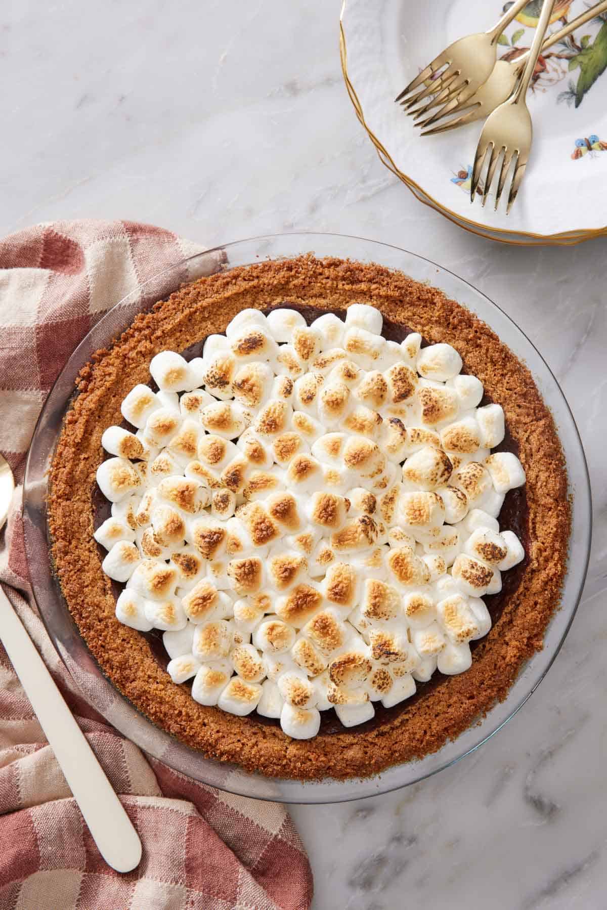 Overhead view of a s'more pie with a stack of plates and forks off to the side.