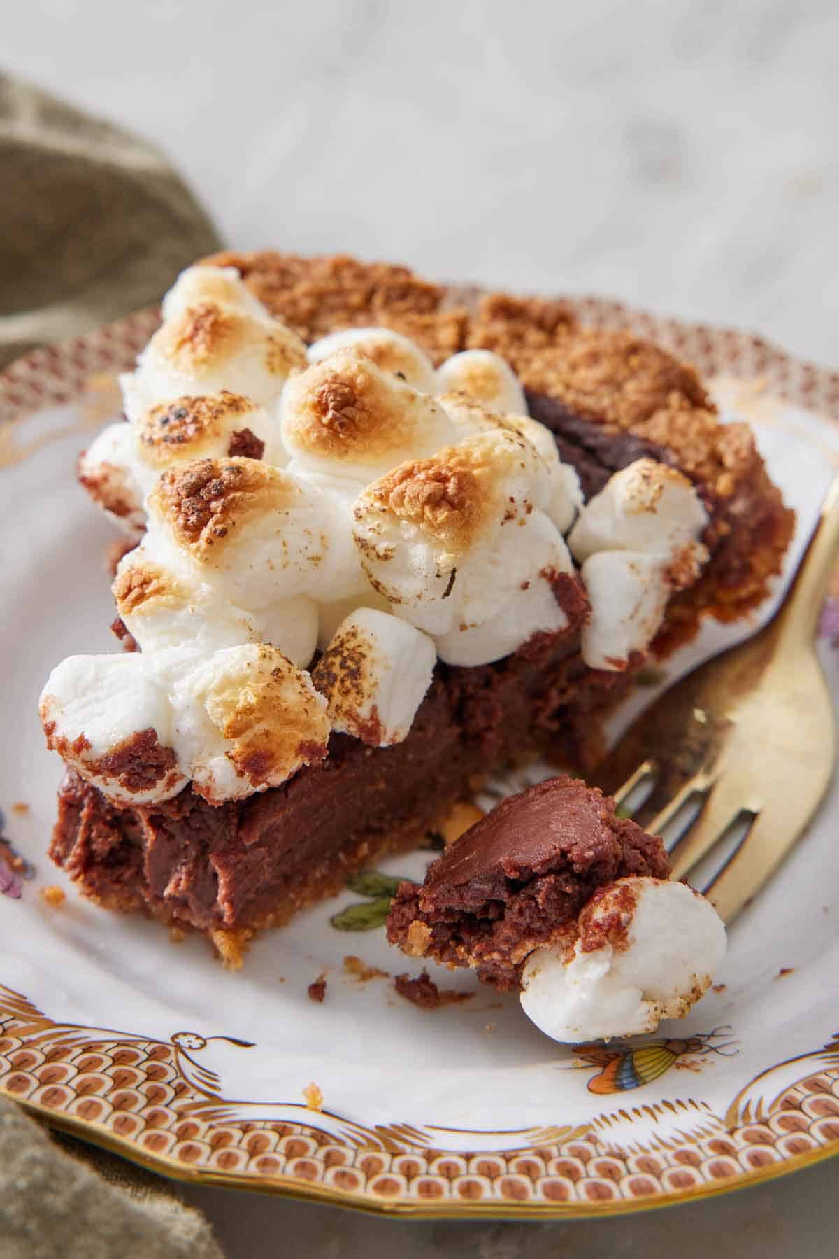 A slice of s'more pie on a plate with a fork with the tip of the pie on it beside the slice.