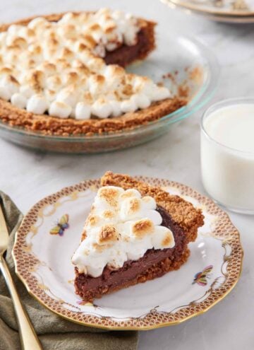 A slice of s'more pie with a glass of milk and the rest of the pie in the background.