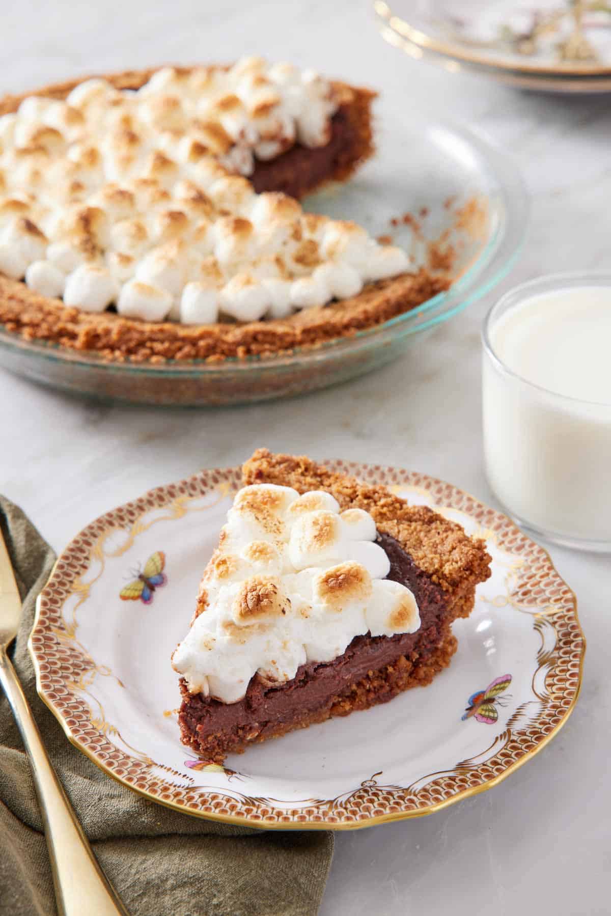 A slice of s'more pie with a glass of milk and the rest of the pie in the background.