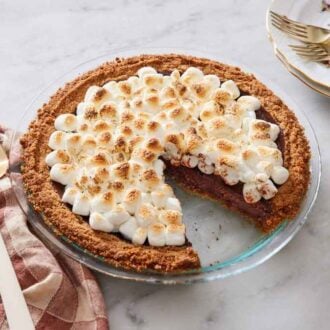A glass pie dish with a s'more pie in it with a slice taken out.