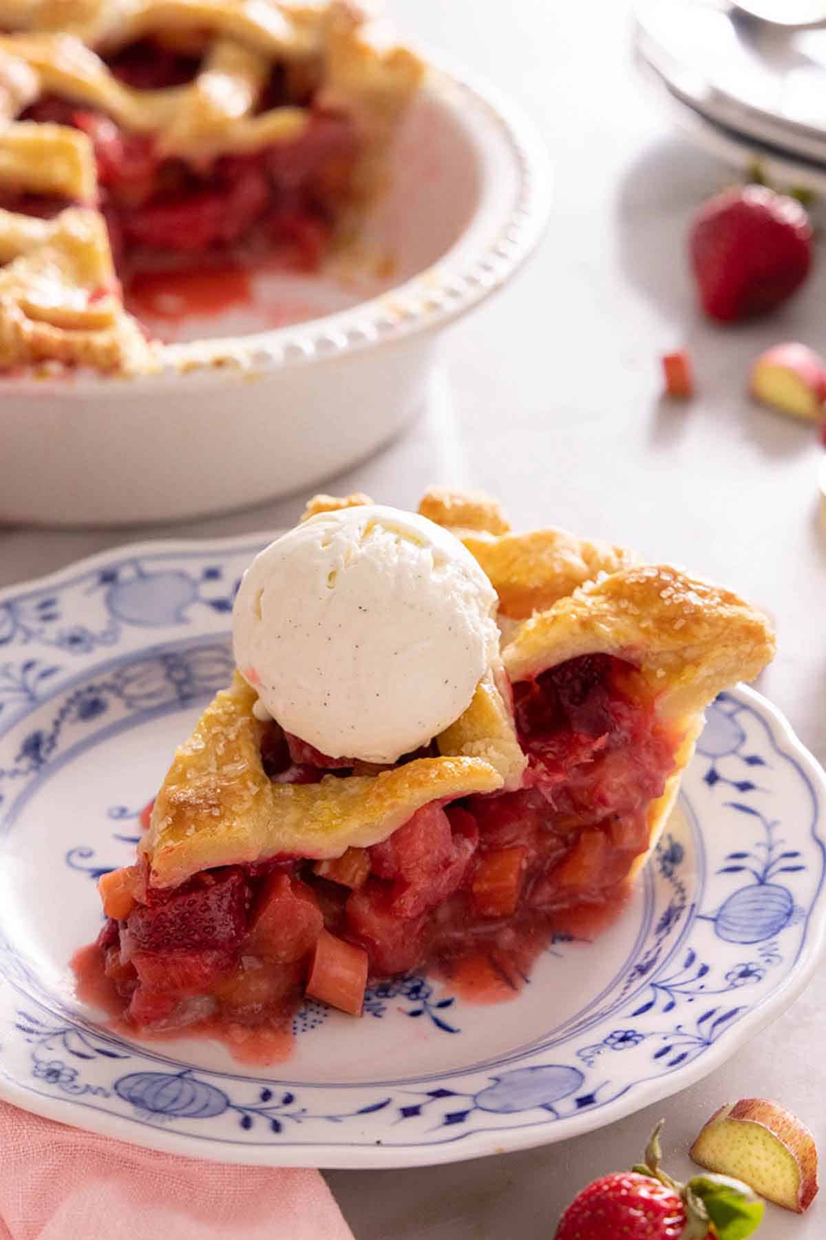 A plate with a slice of strawberry rhubarb pie with a scoop of vanilla ice cream on top.