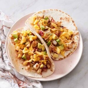 A plate with two breakfast tacos with a napkin beside it.
