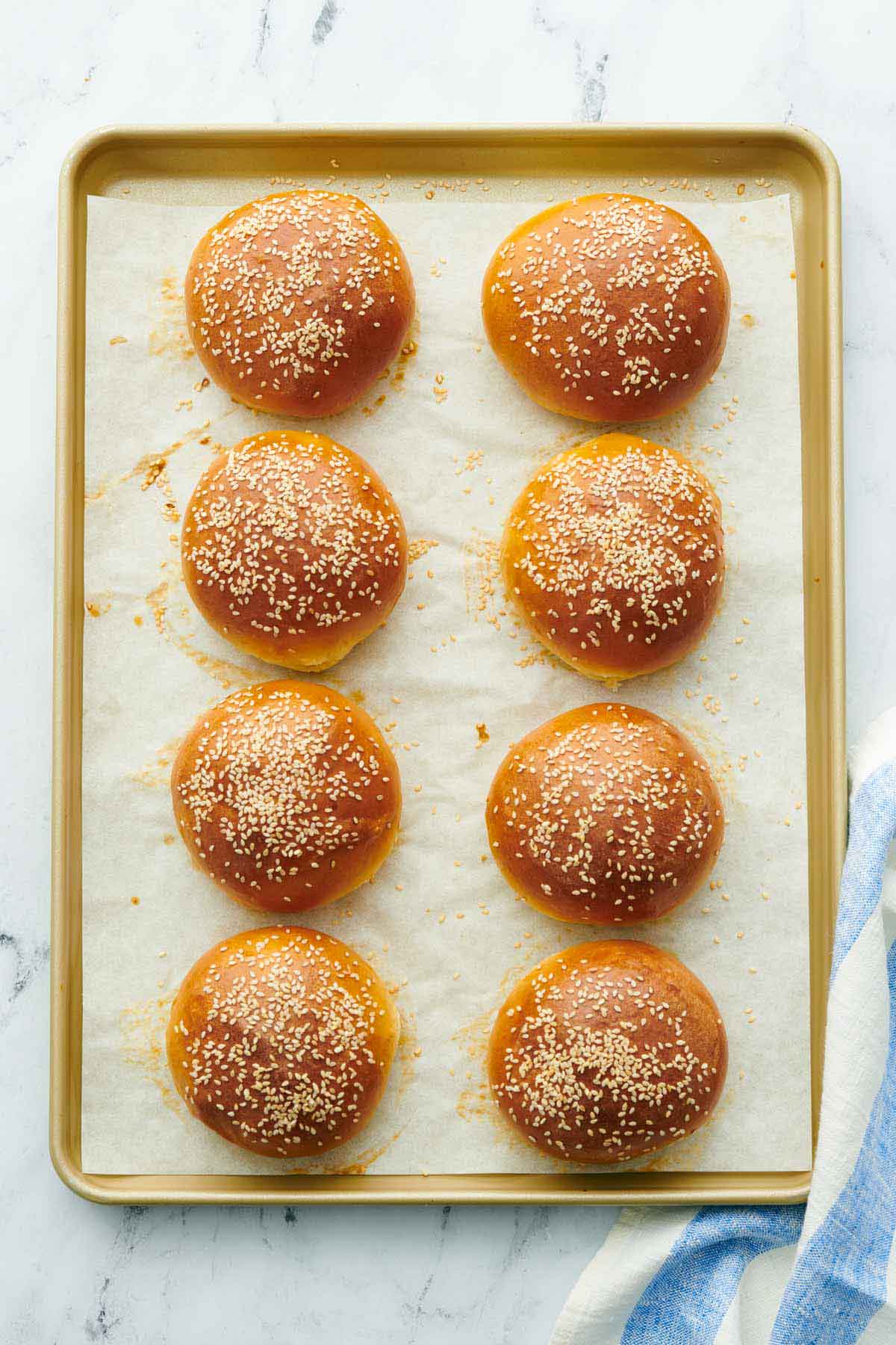 Overhead view of a sheet pan with freshly baked burger buns.