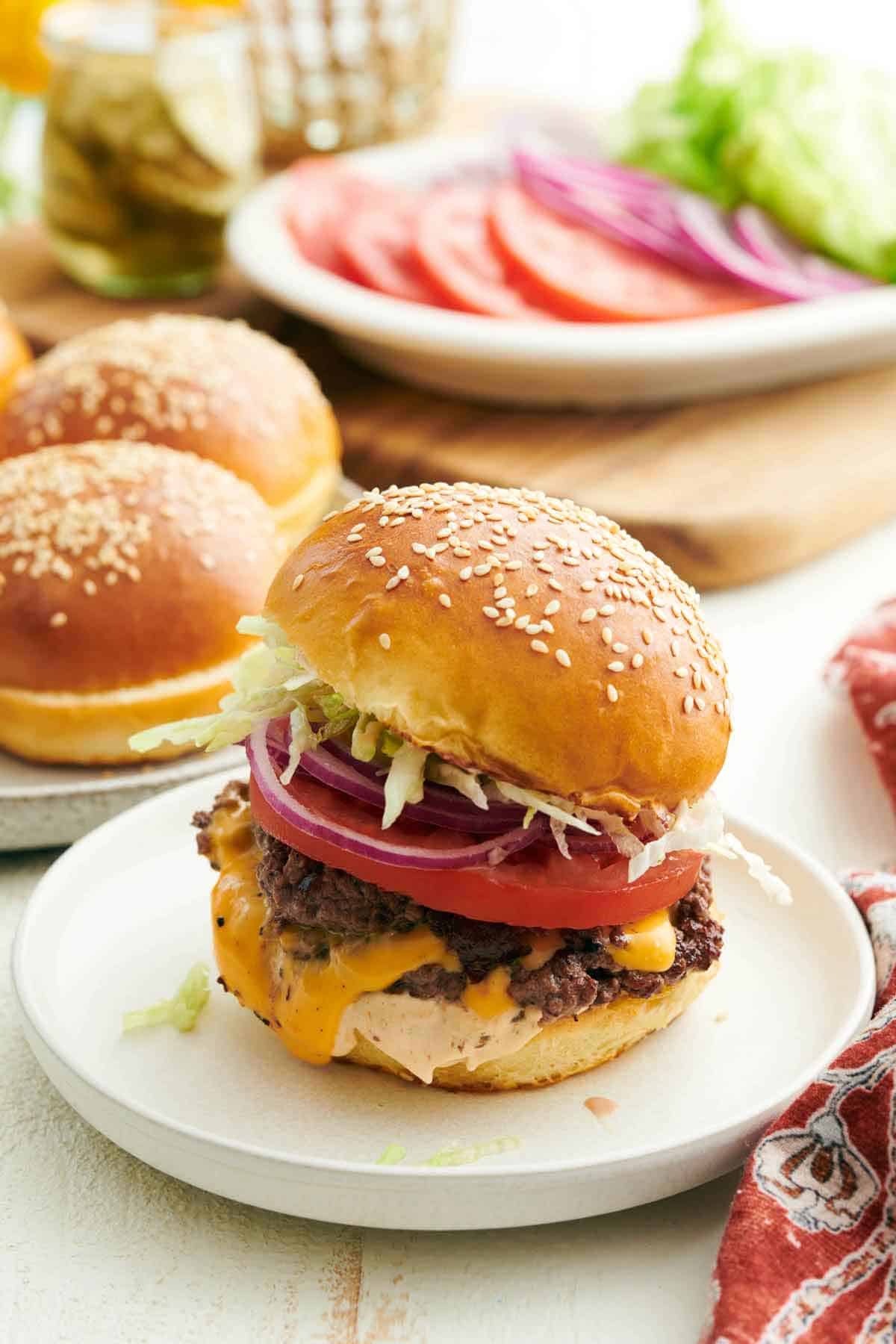 A plate with a burger with homemade burger buns and toppings in the background.