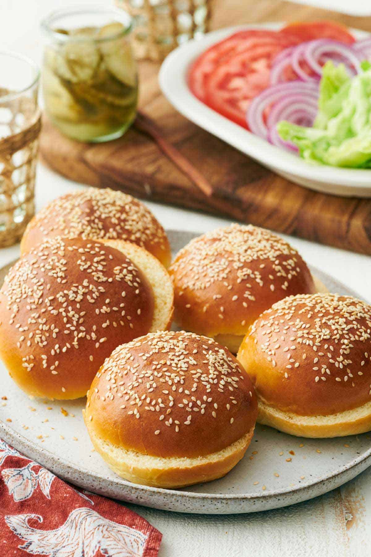 A platter with multiple burger buns. Toppings in the background.