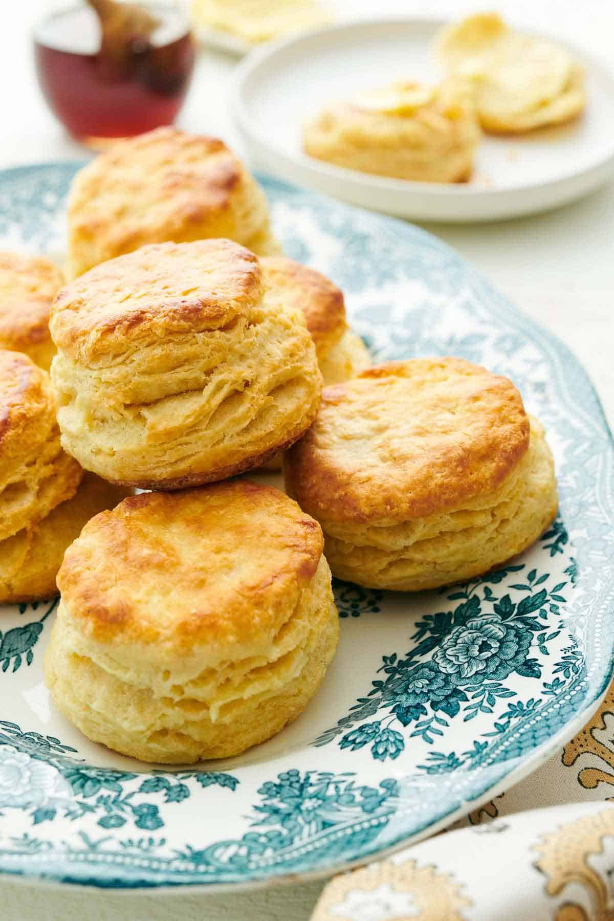 A platter with buttermilk biscuits with honey in the background and another plate.