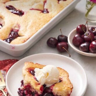 Pinterest graphic of a plate with a serving of cherry cobbler with the rest of the cobbler in the background with a bowl of cherries.