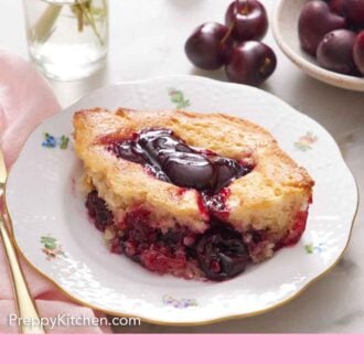 Pinterest graphic of a plate with a serving of cherry cobbler with a small vase of flowers and cherries in the back.