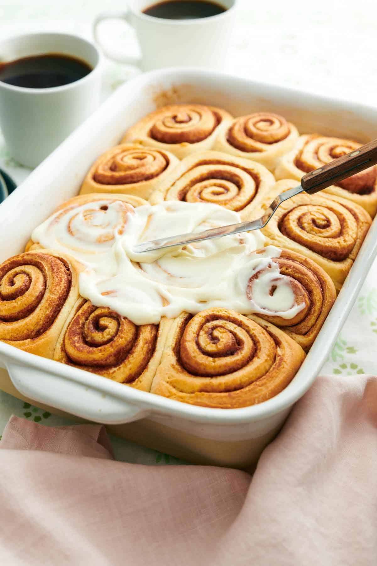 Icing spread on top of cinnamon rolls in a baking dish.