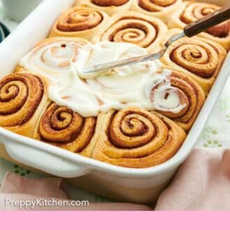 Pinterest graphic of icing spread on top of cinnamon rolls in a baking dish.