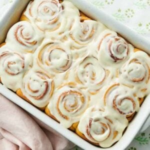 Overhead view of cinnamon rolls with a layer of icing with a mug of coffee and stack of plates on the side.