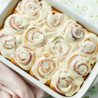 Overhead view of cinnamon rolls with a layer of icing with a mug of coffee and stack of plates on the side.
